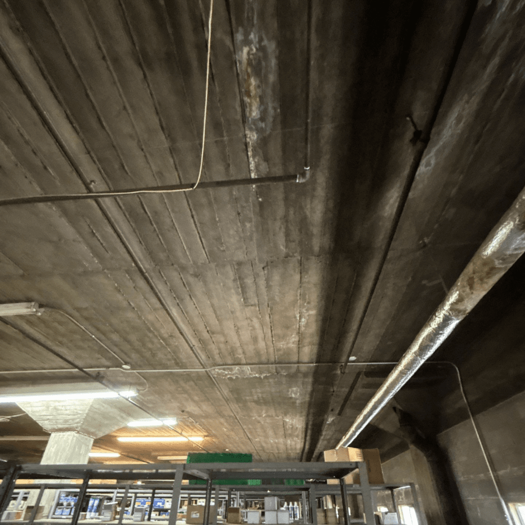 Concrete decking on a low slope as it appears from the interior of an industrial commercial building.