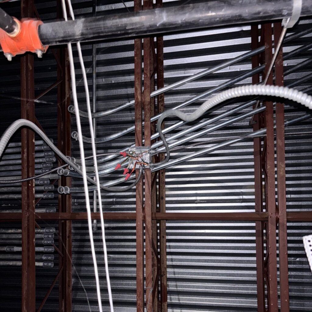 Metal decking on a low slope commercial roof as it appears from the building's interior with visible electrical lines.