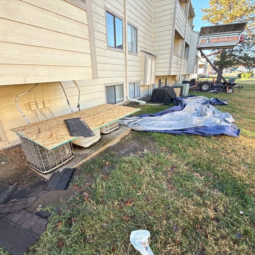 OSB and tarps protecting AC units and surrounding area while an Equipter collects roof debris at a multifamily property.