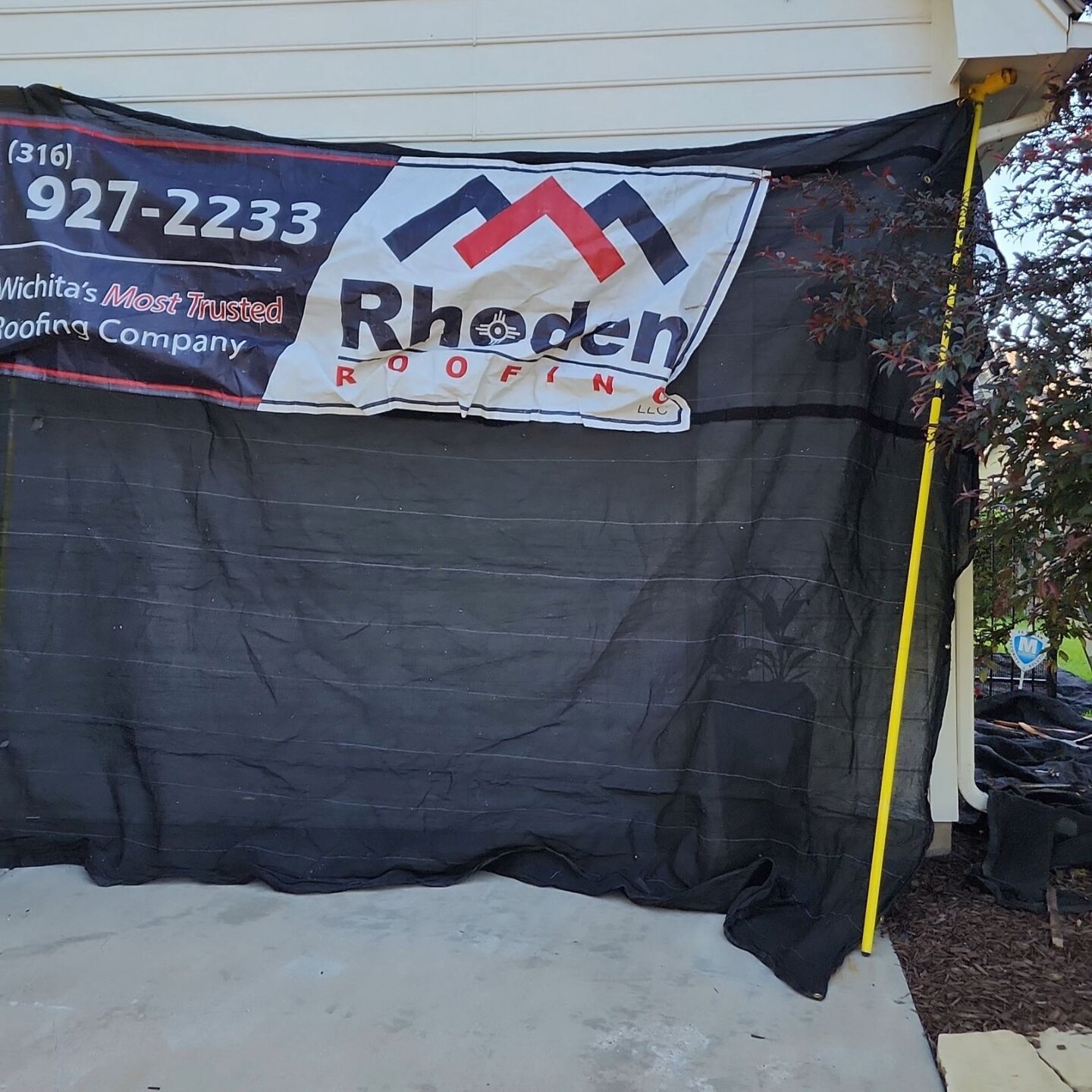 Catch-All mesh system with Rhoden Roofing branding protecting the side of a home during tear-off.