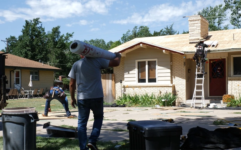 Production Foreman carries roofing material to roofing professionals at a build site.