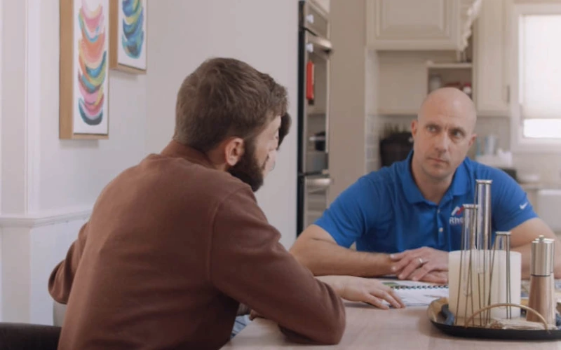 Project Coordinator and customer sitting at a table discussing a roofing project.