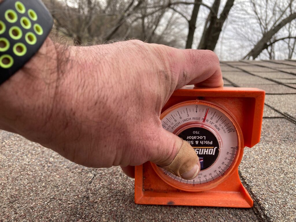 An orange roof level is used by a Project Coordinator to determine an asphalt shingle roof's pitch.