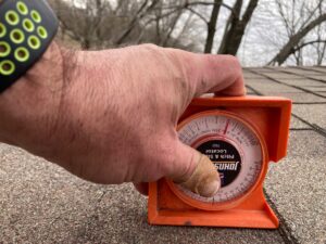 An orange roof level is used by a Project Coordinator to determine an asphalt shingle roof's pitch.