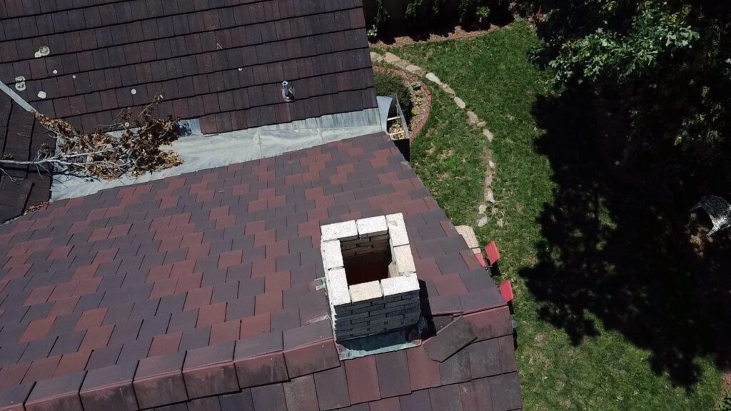 A brick chimney with no chase on a red tile roof.