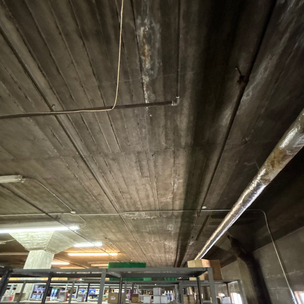 Concrete decking on a low slope as it appears from the interior of an industrial commercial building.