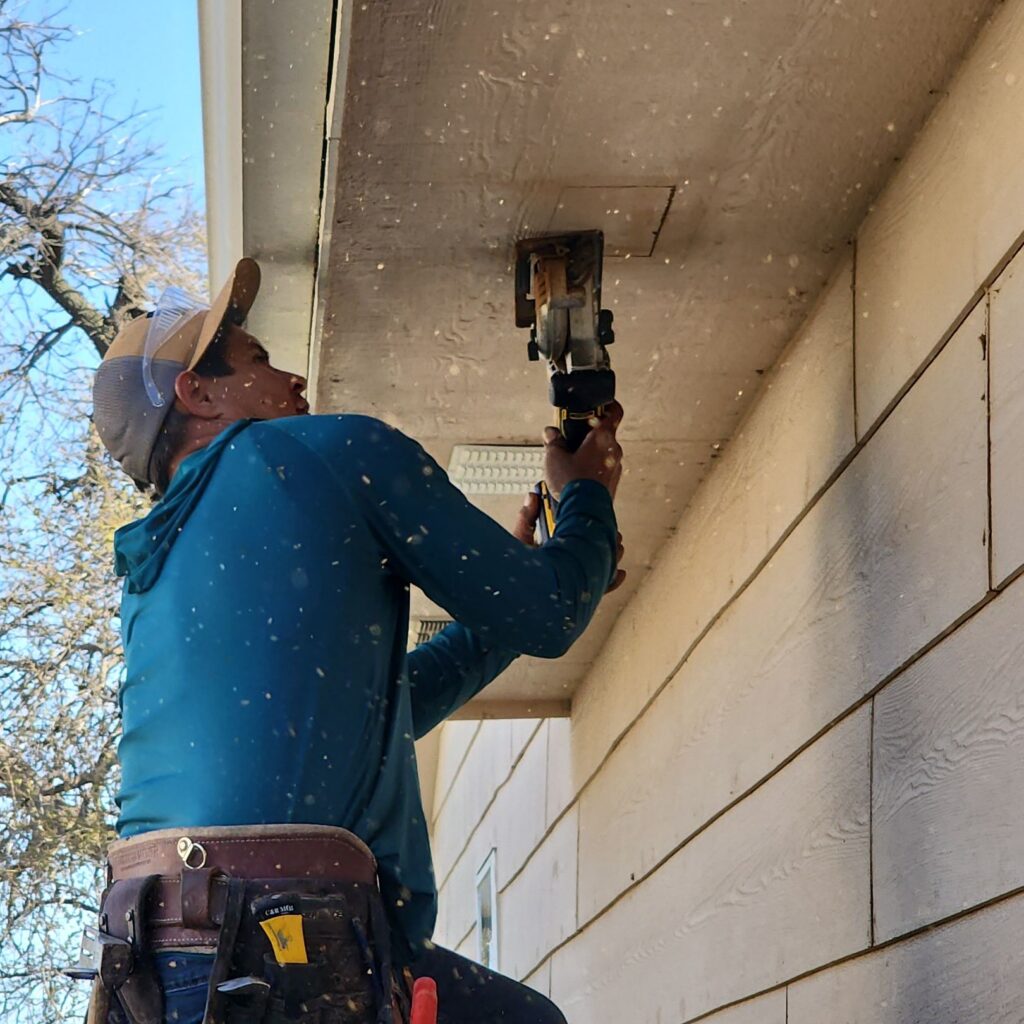 A worker cutting a hole in the soffits to provide air intake for the attic space.