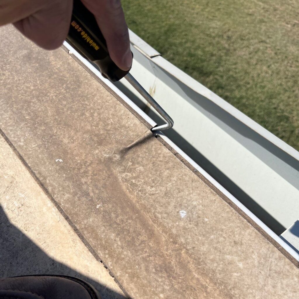 A gab in a low-slope commercial roof's drip edge is highlighted with a probing tool.