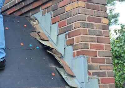 Counterflashing on an asphalt shingle roof during a roof replacement, with caulk from previous repairs visible atop the counterflashing.