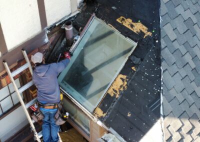 Roofers installing a deck-mounted skylight on an asphalt shingle roof.