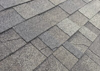 Cracked architectural asphalt shingles, exposing the asphalt layer beneath the granules.