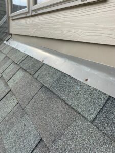 Exposed fasteners on headwall flashing protecting the downslope side of a dormer on an asphalt shingle roof.
