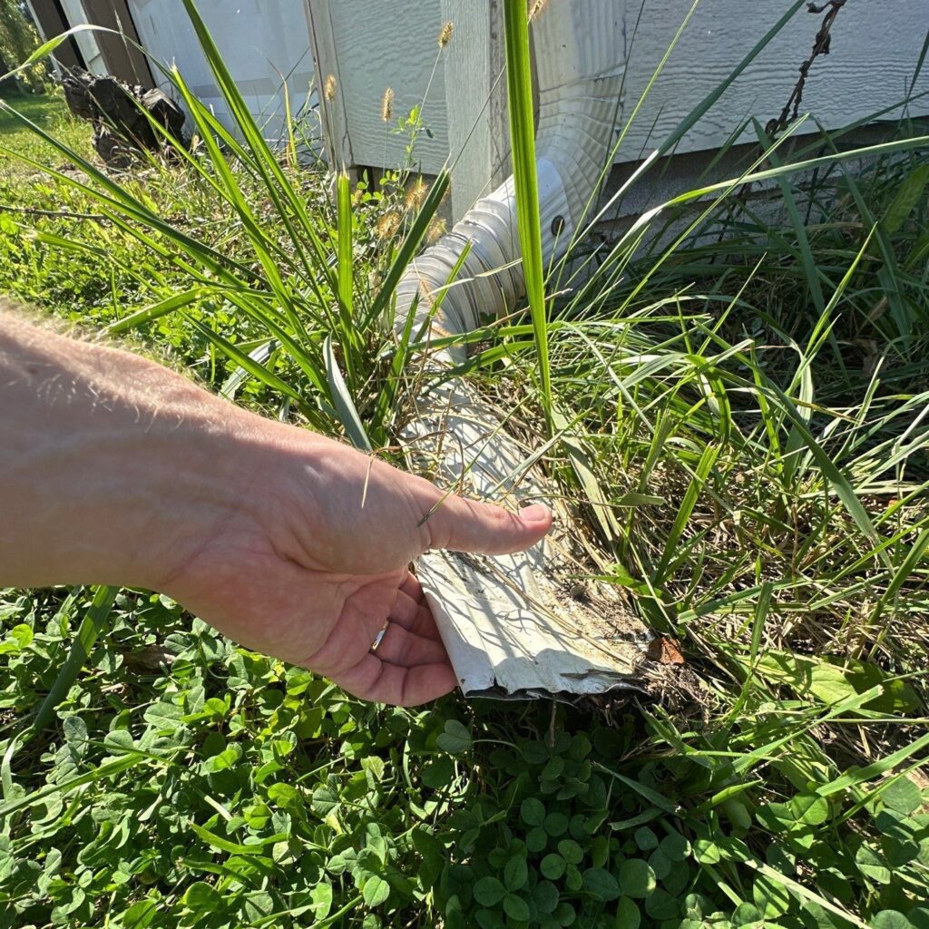 A downspout with a corrugated connector leading to a crushed chute.