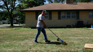 A worker using a magnet roller to catch leftover nails in the yard after a roof replacement.