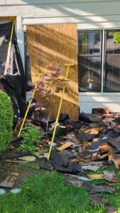 OSB panel propped against siding to protect windows and shrubs during roof tear-off.