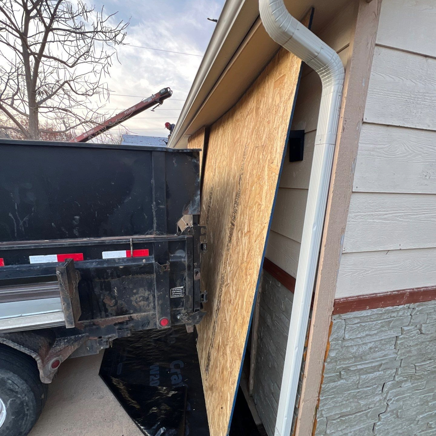 OSB panel protecting a home's garage door next to a dump trailer during a roof tear-off.