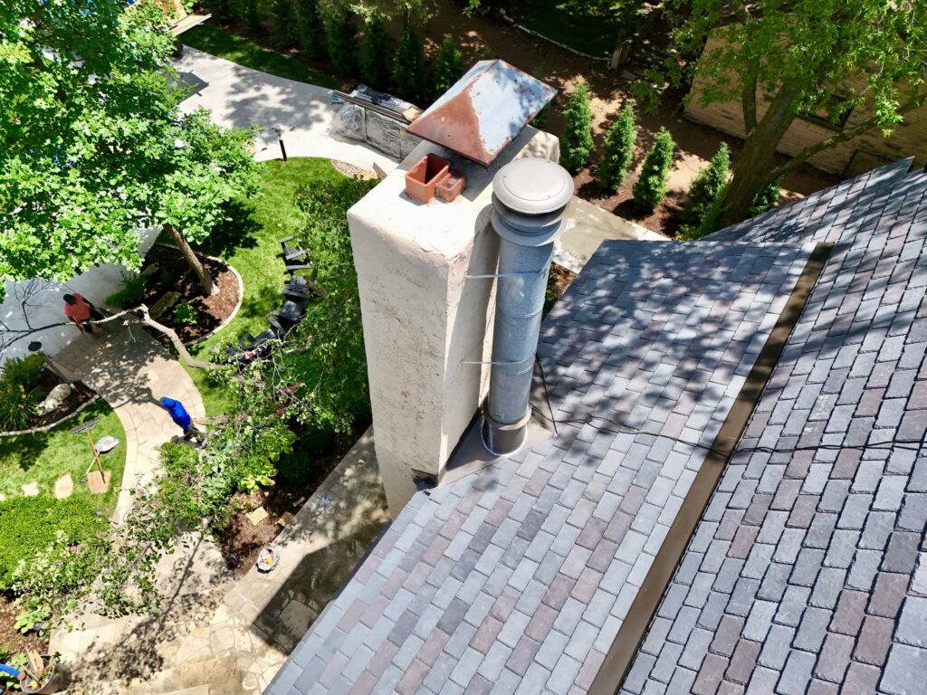 A single piece of custom-fabricated metal flashing protects a large heater flue base and provides the chimney's cricket on a slate tile roof.