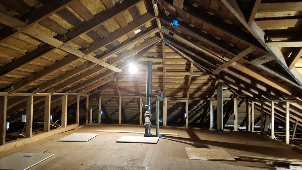 Attic cleared and prepped for a hot-roof conversion, with wiring and roof framing exposed before closed-cell spray foam at the roof deck.