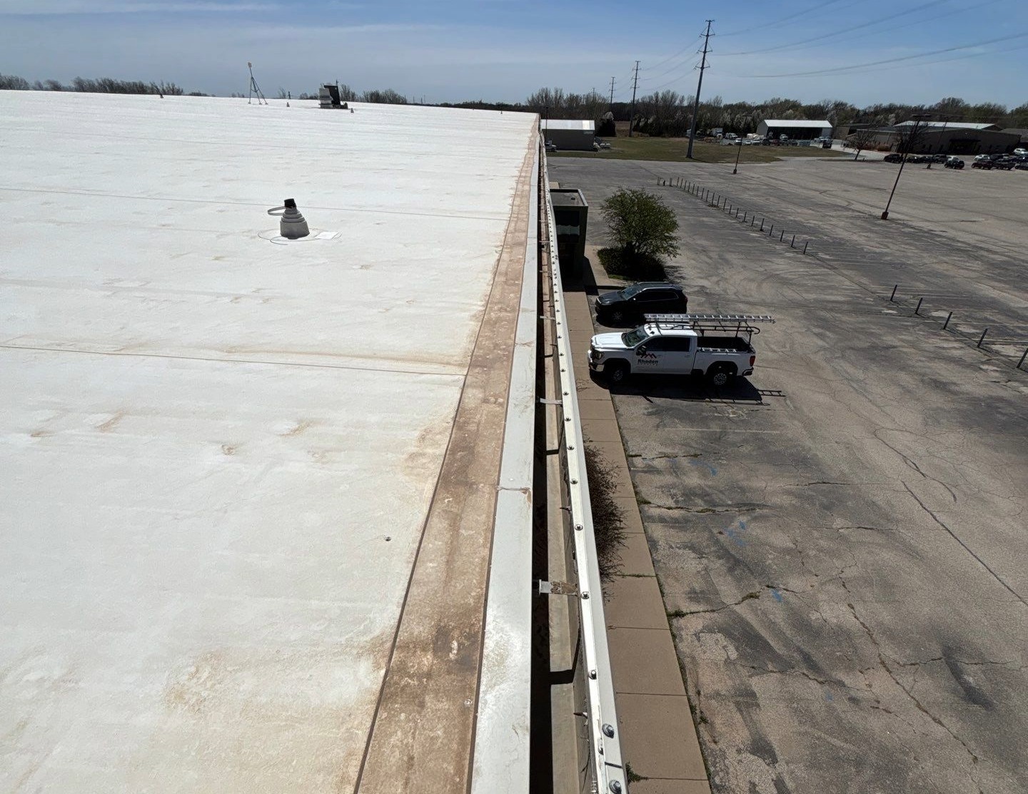Commercial box gutters on a white membrane roof with pipe and communication hardware penetrations and trucks in the parking lot.