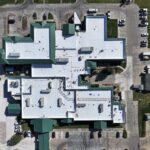 A hospital with a new, white TPO membrane, multiple roof-mounted units and green edge metals.
