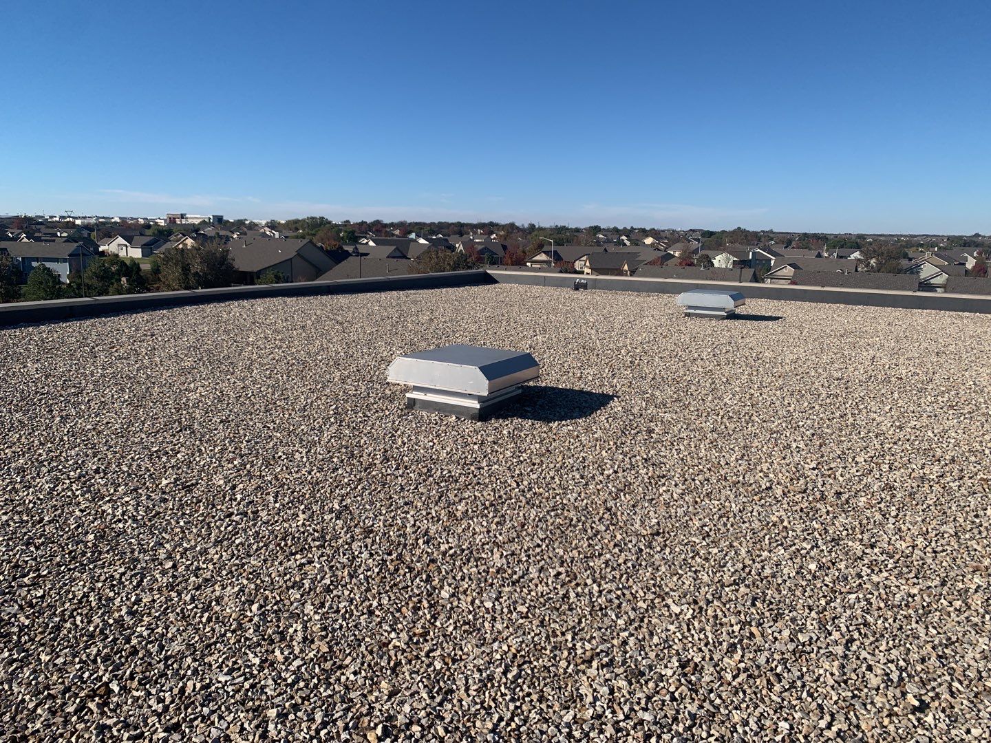 A ballasted roof with a central exhaust hood and blue skies in the background.