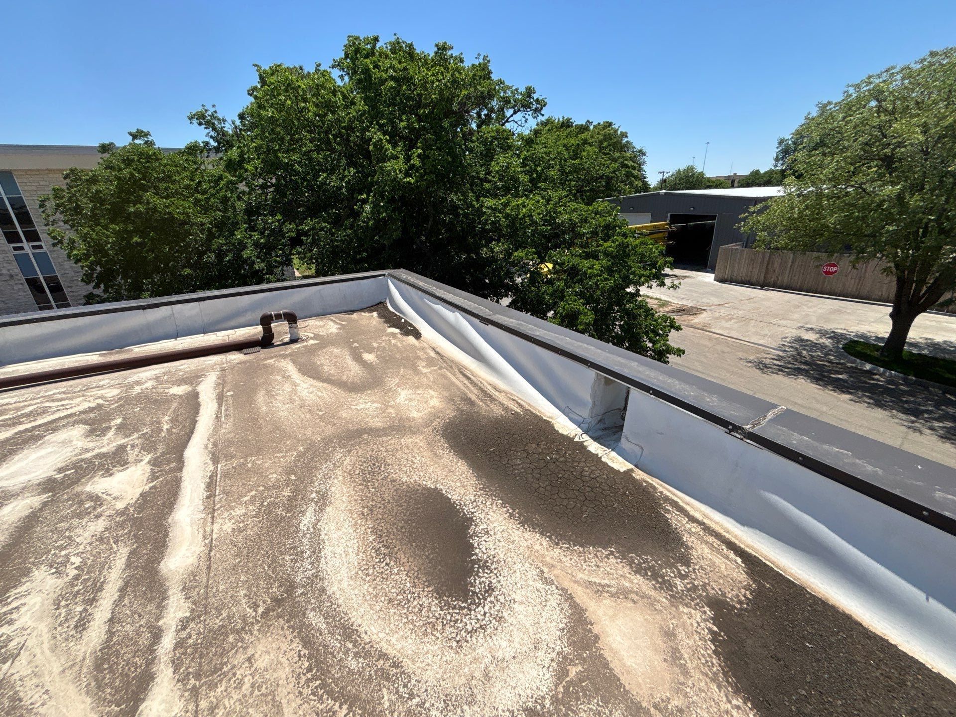 A low-slope commercial roof with bridging (delamination) at the parapet wall near a through-wall scupper.