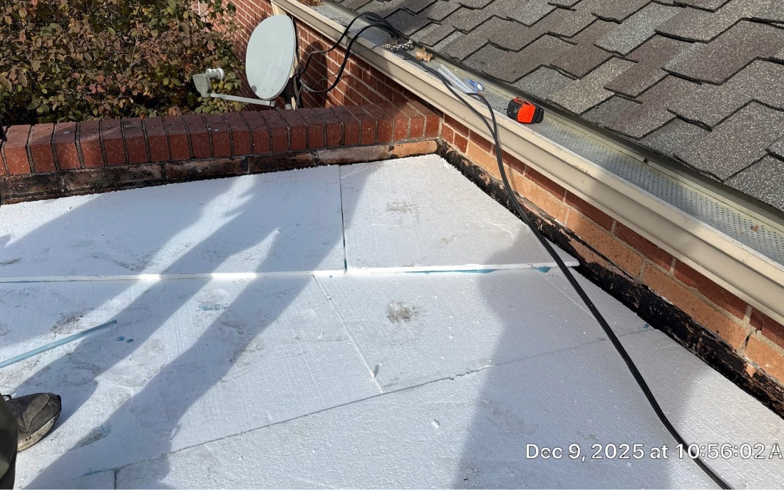 Tapered insulation on a low-slope roof section by a vertical transition to a sloped asphalt roof.