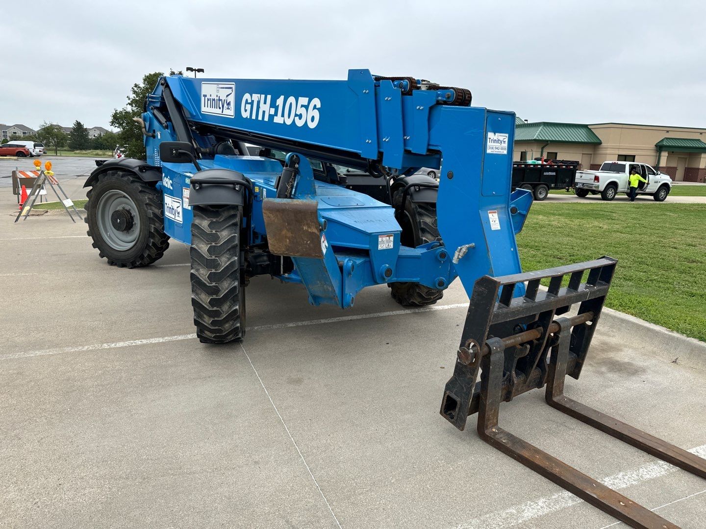 Telehandler A blue telehandler staged in the parking lot of a commercial low-slope building before its roof is replaced.
